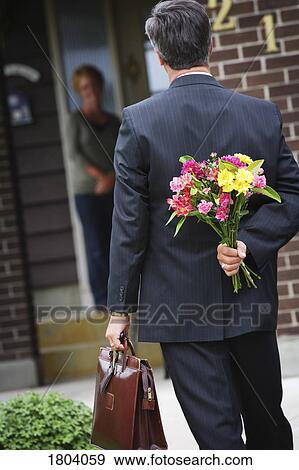 Man holding a bouquet of flowers behind his back for a woman View Large Photo Image Stock Photo - Man holding a bouquet of flowers behind his back for a woman. Fotosearch