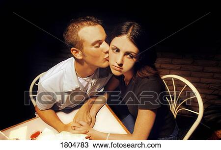 Stock Image - Man kissing an unhappy woman on the cheek. Fotosearch