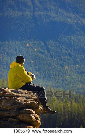 Stock Photo - Man sitting on a mountain in Jasper National Park, Alberta. Fotosearch