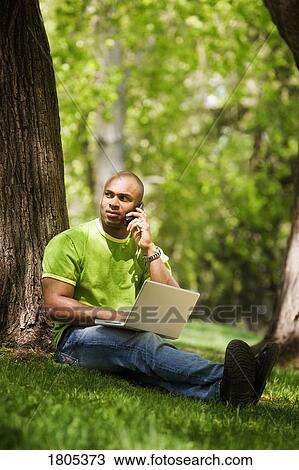 Stock Image - Man talking on mobile with laptop computer. Fotosearch