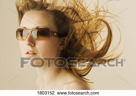Stock Image - Portrait of young woman with hair blowing in air. Fotosearch