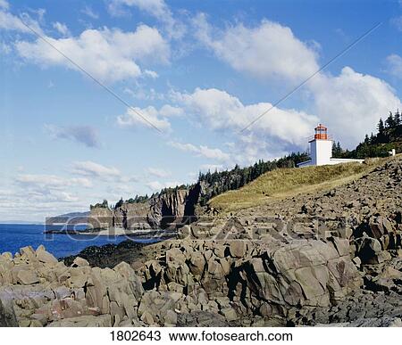 Stock Image - Rocky shoreline with lighthouse. Fotosearch