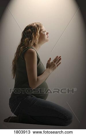 Stock Image - Side view of a pensive pregnant woman sitting in the prayer position. Fotosearch