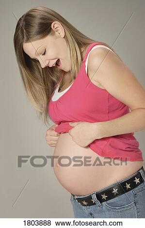 Stock Photo - Side view of a pregnant woman looking at her belly. Fotosearch