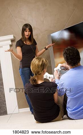 Stock Image - Teenage girl frustrated with couple for playing video game. Fotosearch