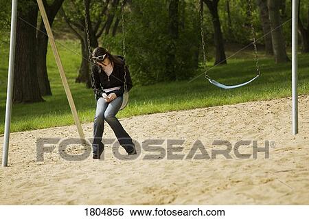 Stock Photograph - Troubled teenager on a swing in the park. Fotosearch