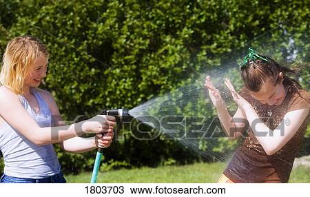 Stock Image - Two teenage girls having a waterfight with hose. Fotosearch