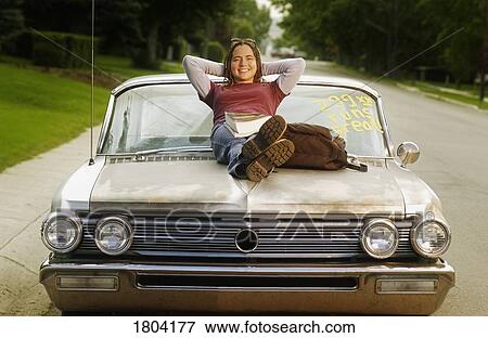 Stock Photo - Woman sitting on the hood of a retro car. Fotosearch