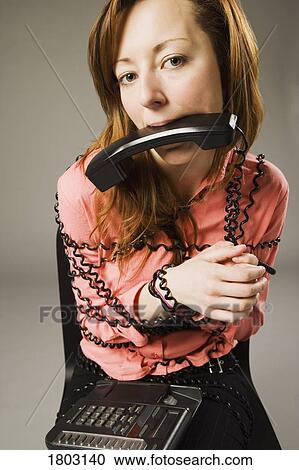 Stock Image - Woman wrapped in telephone cord, holding receiver in mouth. Fotosearch