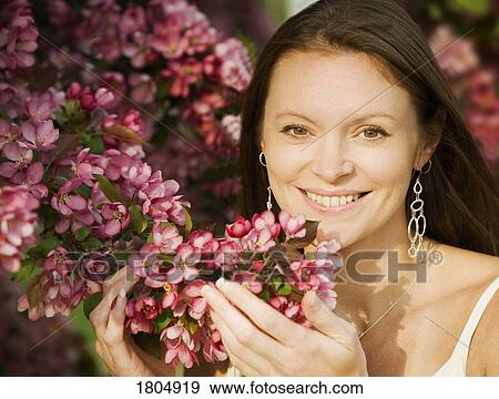 Young woman smiling and smelling flowers View Large Photo Image Stock Photo - Young woman smiling and smelling flowers. Fotosearch