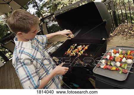 Stock Image - Boy barbecuing outdoors. Fotosearch