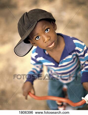 Stock Photograph - Boy wearing over sized hat riding bike. Fotosearch
