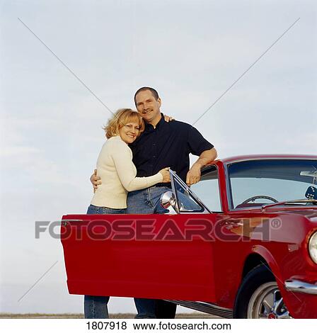 Couple embracing by red car View Large Photo Image Stock Photo - Couple embracing by red car. Fotosearch
