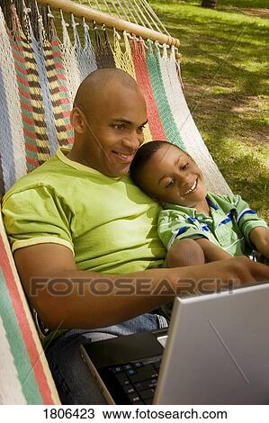 Stock Image - Dad and son in hammock with computer. Fotosearch