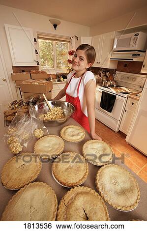 Stock Photograph - Girl standing in kitchen with pies. Fotosearch