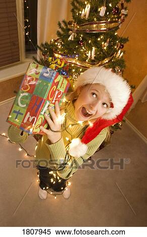 Girl wearing Santa hat and holding Christmas present View Large Photo Image Stock Photography - Girl wearing Santa hat and holding Christmas present. Fotosearch