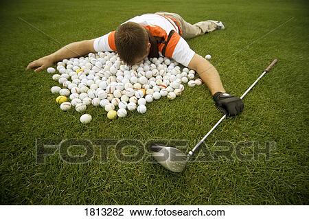 Stock Image - Man lying in pile of golf balls. Fotosearch