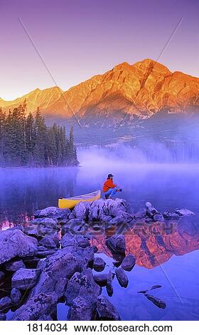 Man sitting on rock with mountains in background View Large Photo Image Picture - Man sitting on rock with mountains in background. Fotosearch