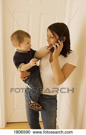 Stock Image - Mother holding son while talking on phone. Fotosearch