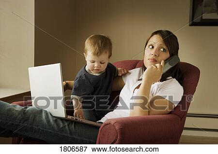 Stock Photo - Mother on the phone with laptop and child on her lap. Fotosearch