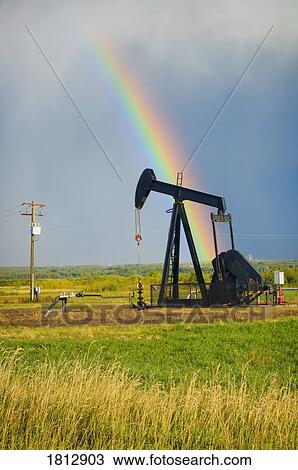 Stock Image - Storm clouds and rainbow over prairie oil pump . Fotosearch