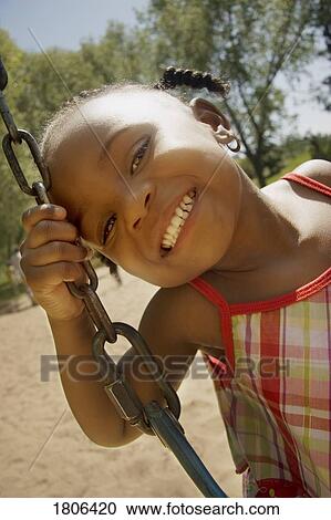 Stock Image - Young girl posing while sitting on a swing. Fotosearch