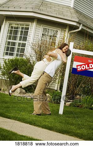 Stock Photo - A couple beside a sold sign in front of a house. Fotosearch