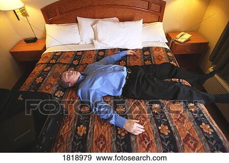 Stock Photo - A man laying on a bed in a hotel room. Fotosearch