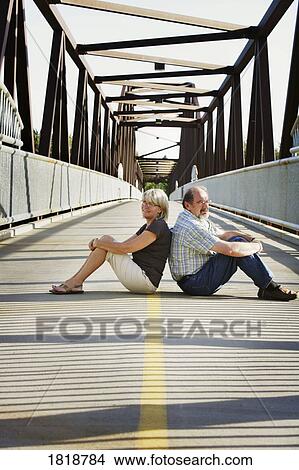 Husband and wife sitting on the middle of a bridge View Large Photo Image Picture - Husband and wife sitting on the middle of a bridge. Fotosearch