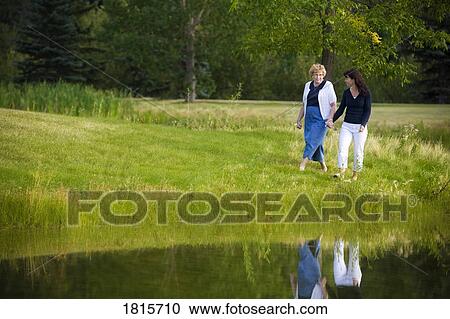 Two women walking beside a lake View Large Photo Image Stock Image - Two women walking beside a lake. Fotosearch