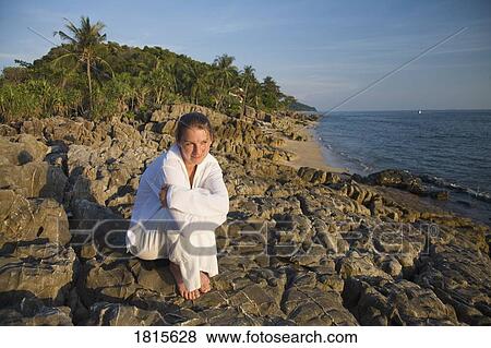 Stock Photo - Woman sitting on rocky shoreline. Fotosearch