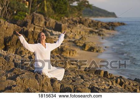 Picture - Woman with arms raised on rocky shoreline. Fotosearch