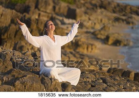 Stock Photography - Woman worshipping on rocky shore. Fotosearch