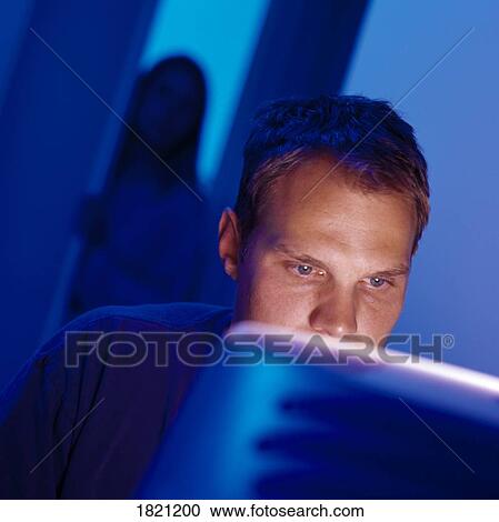 Stock Image - Man working at computer with woman watching him. Fotosearch