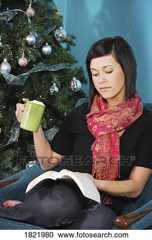 Stock Image - Woman reading by Christmas tree. Fotosearch