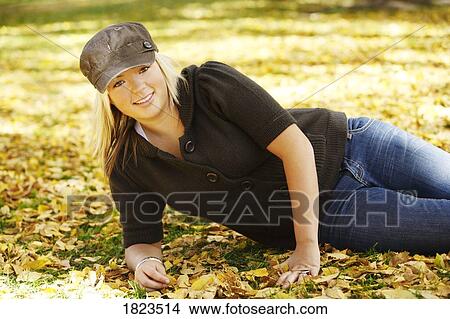 Picture - Teenage girl lying on in the fall leaves. Fotosearch