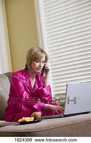 Stock Photo - Woman in pajamas, on the phone and working on laptop computer. Fotosearch