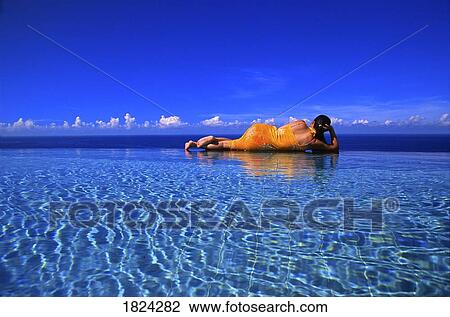 Stock Image - Woman in swimming pool overlooking ocean, Bali, Indonesia. Fotosearch
