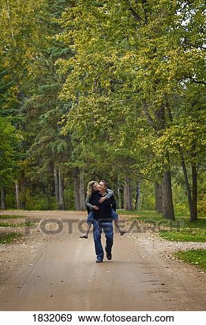 Stock Photo - A husband giving his wife a piggy-back ride . Fotosearch