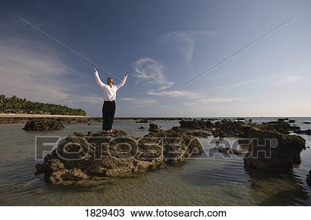 Stock Image - A man on a rock with arms outstretched. Fotosearch