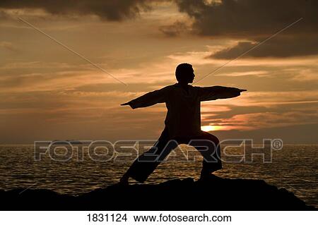 Picture - A man stretching on a beach in Koh Lanta, Thailand. Fotosearch