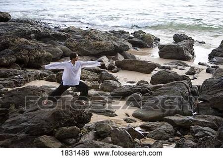 Stock Photograph - A man stretching on a rocky beach in Koh Lanta, Thailand. Fotosearch