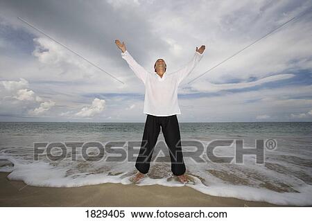 Stock Photography - A man with arms outstretched on a beach in Koh Lanta, Thailand. Fotosearch