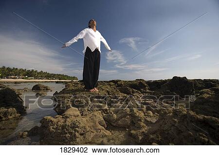 A man with arms outstretched on a rocky beach View Large Photo Image Stock Image - A man with arms outstretched on a rocky beach. Fotosearch