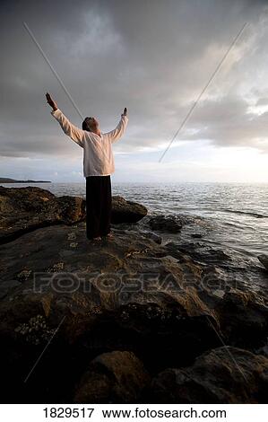 Stock Photo - A person with arms raised on a beach at sunset. Fotosearch
