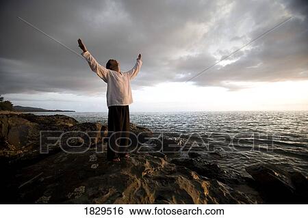 Stock Photograph - A person with arms raised on a beach at sunset, Koh Lanta, Thailand, Asia. Fotosearch