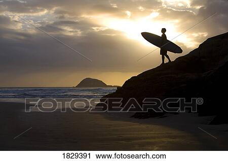 Stock Image - A surfer on Muriwai Beach, New Zealand. Fotosearch