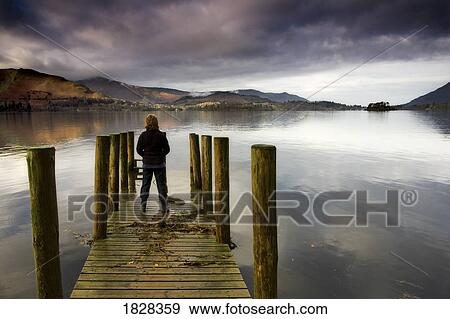 Stock Photo - A woman standing on a wooden pier, Lake Derwent, Cumbria, England. Fotosearch