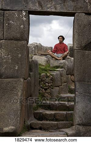 Picture - A young man meditates in ancient Incan ruins outside Cuzco, Peru. Fotosearch