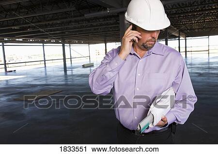 Stock Image - Architect with blueprint and cell phone. Fotosearch